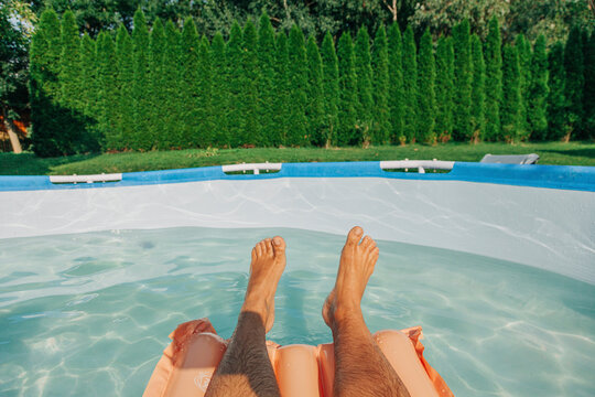 Legs of man floating in wading swimming pool at backyard