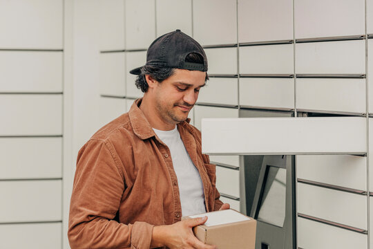 Smiling man wearing brown shirt holding delivery package near locker