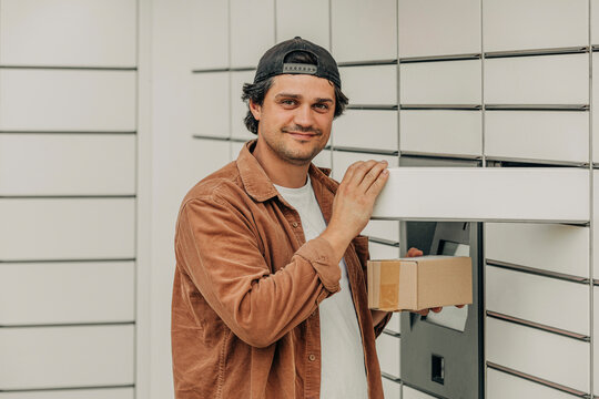 Happy man wearing brown shirt holding delivery package near locker