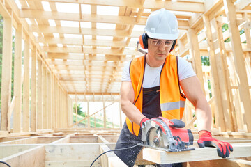 Front view of craftsman, builder standing, looking down, cutting wodden gilder by professional equipment. Builder wearing yellow vest, helmet, glasses working. Concept of building.