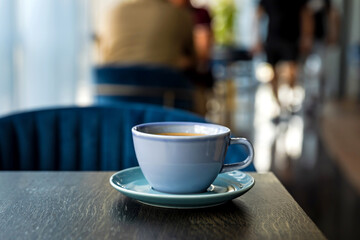 Blue ceramic cup of hot black coffee on wooden table, cafe atmosphere, people in bokeh, copy space - 644374281