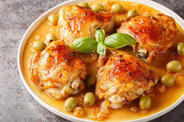 Fragrant hot ruddy chicken thighs baked with green olives close-up in a plate on the table. Horizontal