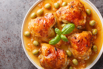 Mediterranean chicken thigh baked with green olives and onion paprika sauce close-up in a plate on the table. Horizontal top view from above