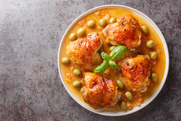 Homemade chicken thigh with crispy skin baked with green olives and onion paprika sauce close-up in a plate on the table. Horizontal top view from above