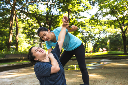 Fatwoman feeling back pain during exercise in park and sportswoman freind helping