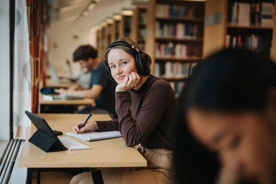 Portrait of smiling student wearing headphones while studying in library at university