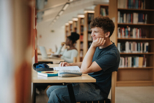 Side view of smiling student sitting with hand on chin in library