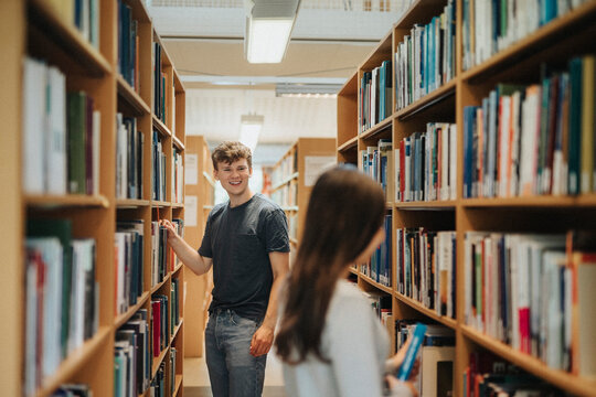 Happy students searching books on bookshelf in library at university