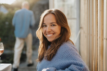 Side view portrait of smiling woman wearing sweater during dinner party at cafe