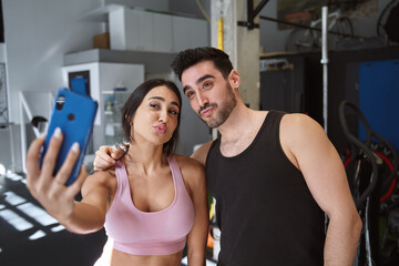 brunette fitness couple taking a selfie with their cell phone smiling after finishing their workout