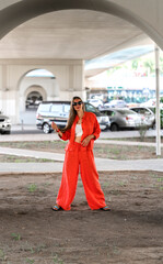 Obraz premium Summer portrait of a girl with long blond hair. A girl in orange clothes and sunglasses stands on the street.