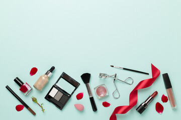 Flat lay with makeup products and tools with flowers on color background