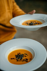 Man carrying a two plates of pumpkin soup in a white bowl