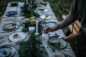 Woman setting up the table. The table is elegantly set with crisp white tablecloths, sparkling glassware, and polished silverware
