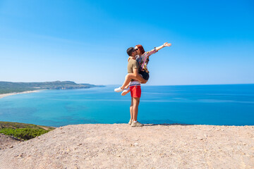 Young guy and girl travelers are kissing on a panoramic background of the sea. Sardinia Italy