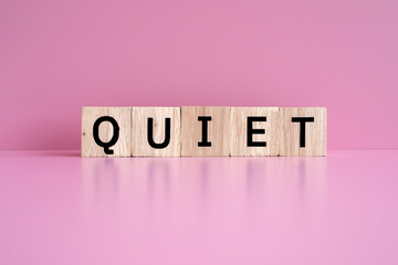Wooden blocks form the text "QUIET" against a pink background.