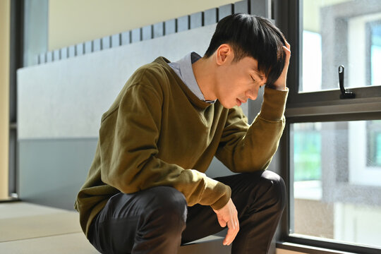 Unhappy young man holding his head, suffering from depression. Loneliness, depression, mental heath concept