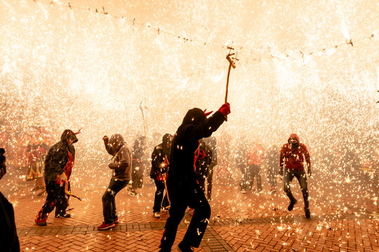 People in costumes with pitchforks spraying fireworks during festival at night