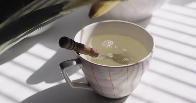 Morning routine. Close-up of a cup and hands pouring water from a teapot, dipping the tea bag and adding a teaspoon of honey.