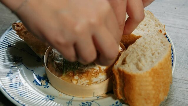 Hand Breaking and Dipping Baguette in Freshly Baked French Camembert Cheese