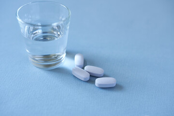 Fototapeta na wymiar White pills and a glass of water on a blue background. Focus on foreground, soft bokeh.