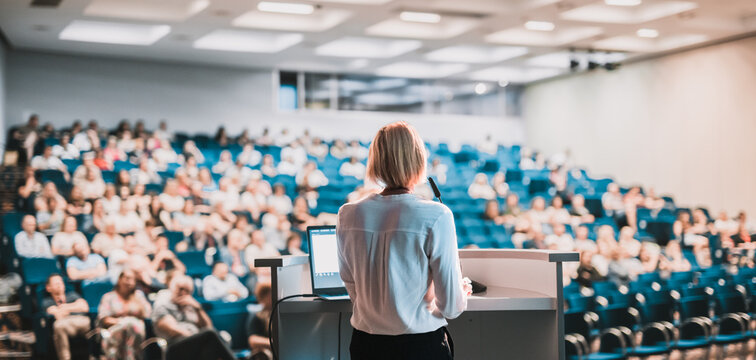 Female speaker giving a talk on corporate business conference. Unrecognizable people in audience at conference hall. Business and Entrepreneurship event
