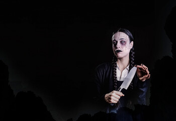A woman with long braids, with gothic and dark look, plays with a butcher knife with her hand, in a...