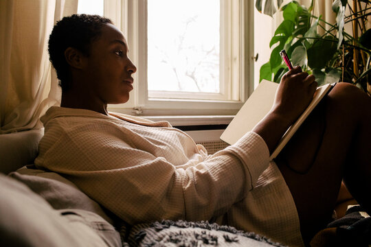 Woman Writing In Book While Reclining On Bed At Home