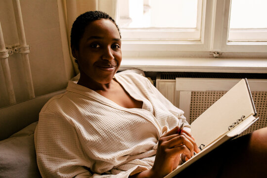 Portrait of smiling young woman with book in bedroom at home