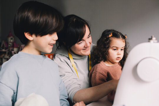 Smiling mother with son and daughter looking at sewing machine