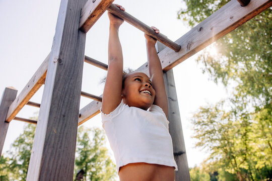 Low angle view of smiling girl hanging while doing monkey bars at summer camp