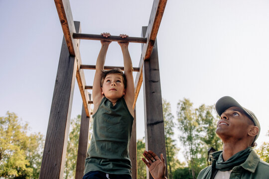 Male camp counselor assisting boy doing monkey bars at summer camp