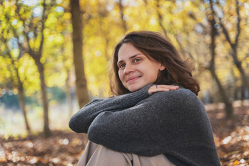 Portrait of young woman in a sweater enjoying the beauty of nature and the sun sitting in the autumn park