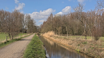 Hiking trail along a draining channel in nature on a sunny spring day in Schoonaarde, Flanders, Belgium