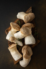 Pleurotus eryngii mushrooms on a cutting board with thyme on a brown background, tasty healthy...