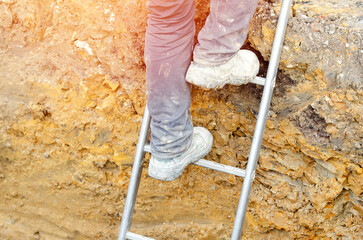 Builder going up the ladder to get out of trench © Iryna