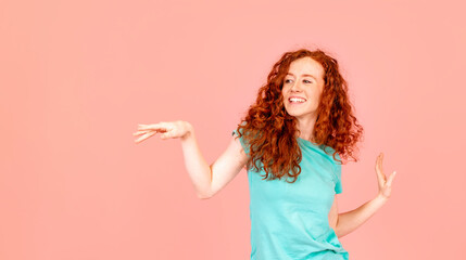 Portrait of a  happy woman with long red hair dancing in green t-shirt on pink background Lifstyle...