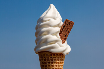 A close up of an ice cream cone with a chocolate flake against a blue sky