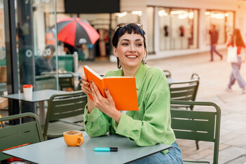 woman student writing in a notebook, making a plan at the street cafe in city. Concept of study...