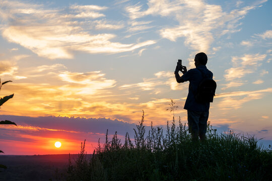 Silhouette of unrecognizable man photographing a beautiful sunset with a smartphone. Selective focus