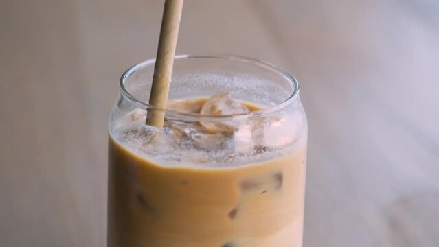 Close up of man mixing iced latte in a glass with a straw on cafe table. Cold summer refreshment drink. Coffee break