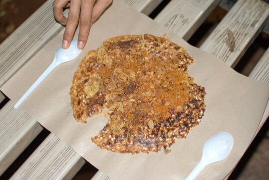 Traditional Indonesian kerak telor street food served on paper plate, crispy egg and sticky rice topped with fried shallots and spices, authentic Betawi culinary heritage.