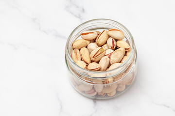 Fresh salted Pistachio nuts into a glass jar isolated on marble background. Top view.