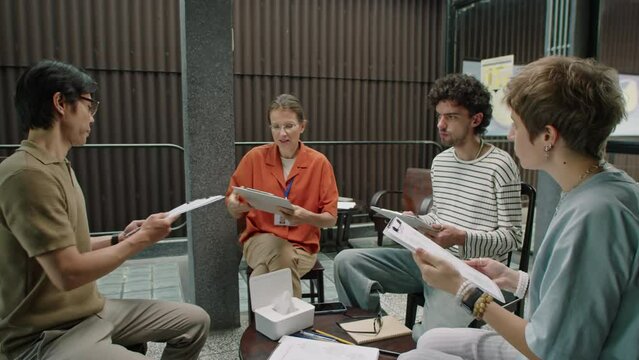 Female psychologist giving clipboards with questionnaires to patients before group therapy session in clinic