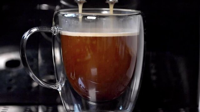 A modern coffee machine pours delicious coffee into a transparent cup standing on a metal support, close-up. Coffee.