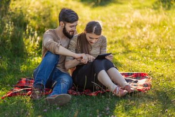 A young couple sits in nature and looks at something in a tablet