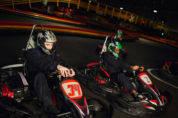 focused multicultural racers driving go kart cart on indoor circuit, speed racing and motorsport