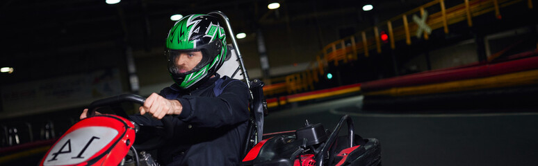 focused racer in helmet and sportswear driving go kart on indoor circuit, adrenaline concept, banner