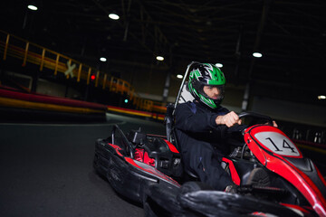 focused racer in helmet and sportswear driving go kart on indoor circuit, adrenaline concept