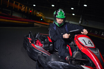 emotional racer in helmet and sportswear driving go kart on indoor circuit, adrenaline concept